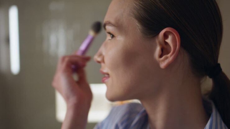 Stylish girl brushing face applying powder closeup. Young woman getting ready
