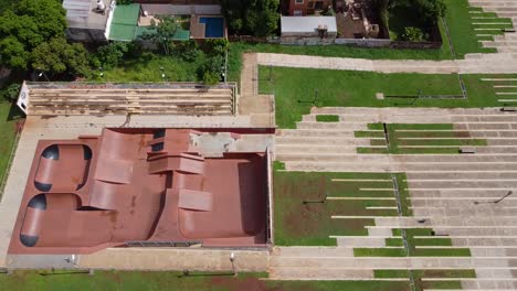 drone wide look-down fly-by de un parque de skate vacío y el parque circundante en la carretera adyacente
