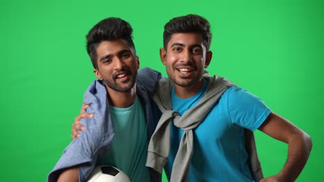 portrait of happy middle eastern football fans rejoicing clapping gesturing victory hugging on green screen. two excited men cheering at chromakey background looking at camera watching match.