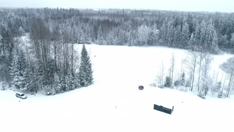 Aerial-descend-across-snowy-field-clearing-in-pine-tree-forest