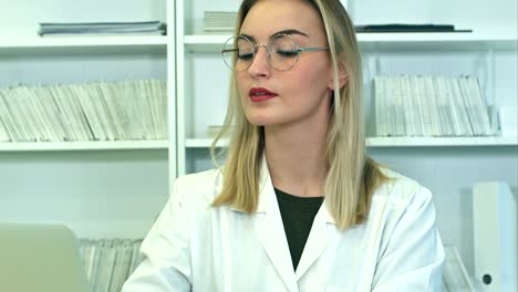 atractiva mujer médica con gafas usando portátil sentada en el escritorio de recepción