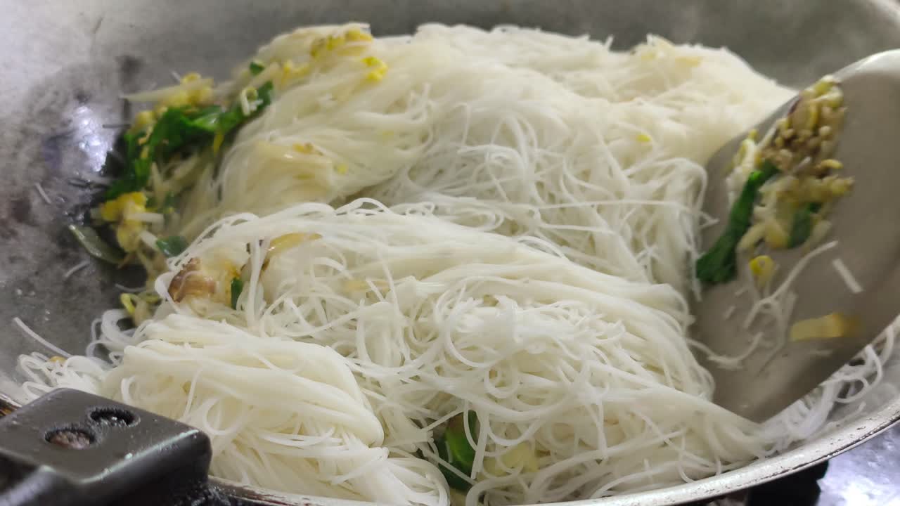 Chef is frying bihun (rice vermicelli) mixed with vegetables, egg, and spices. This flavourful dish is a popular Malaysian food, often served as a quick meal