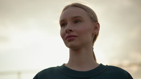 a lady in a green top with pink lips looks thoughtfully towards the horizon under a glowing sky, captured in a peaceful moment of contemplation, with sunlight glowing around her