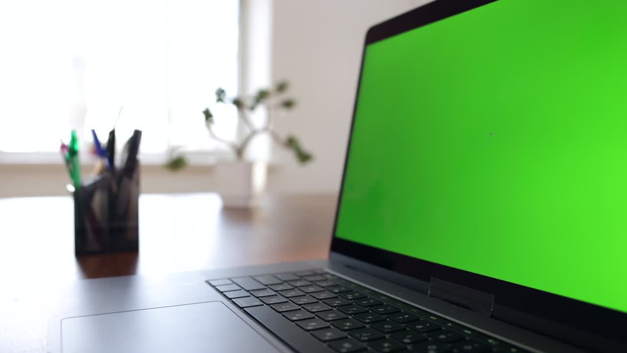 una computadora portátil de pantalla verde sentada en un escritorio de trabajo en casa.