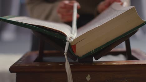 close up of muslim woman praying putting prayer beads into copy of the quran at home