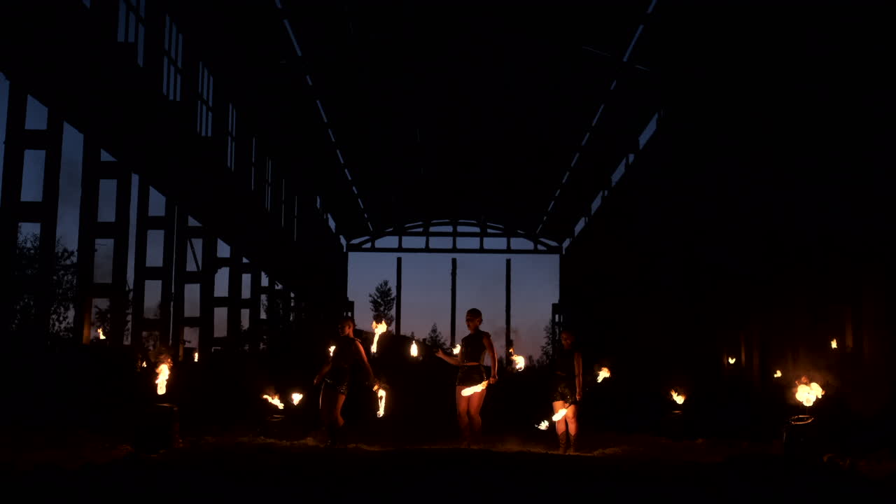 группа людей с огнем и факелами танцует на закате в ангаре в медленном движении.