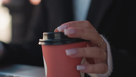 close-up of hand delicately holding a red coffee cup with a meticulous grip, showcasing a serene moment of beverage enjoyment in a soft focus background