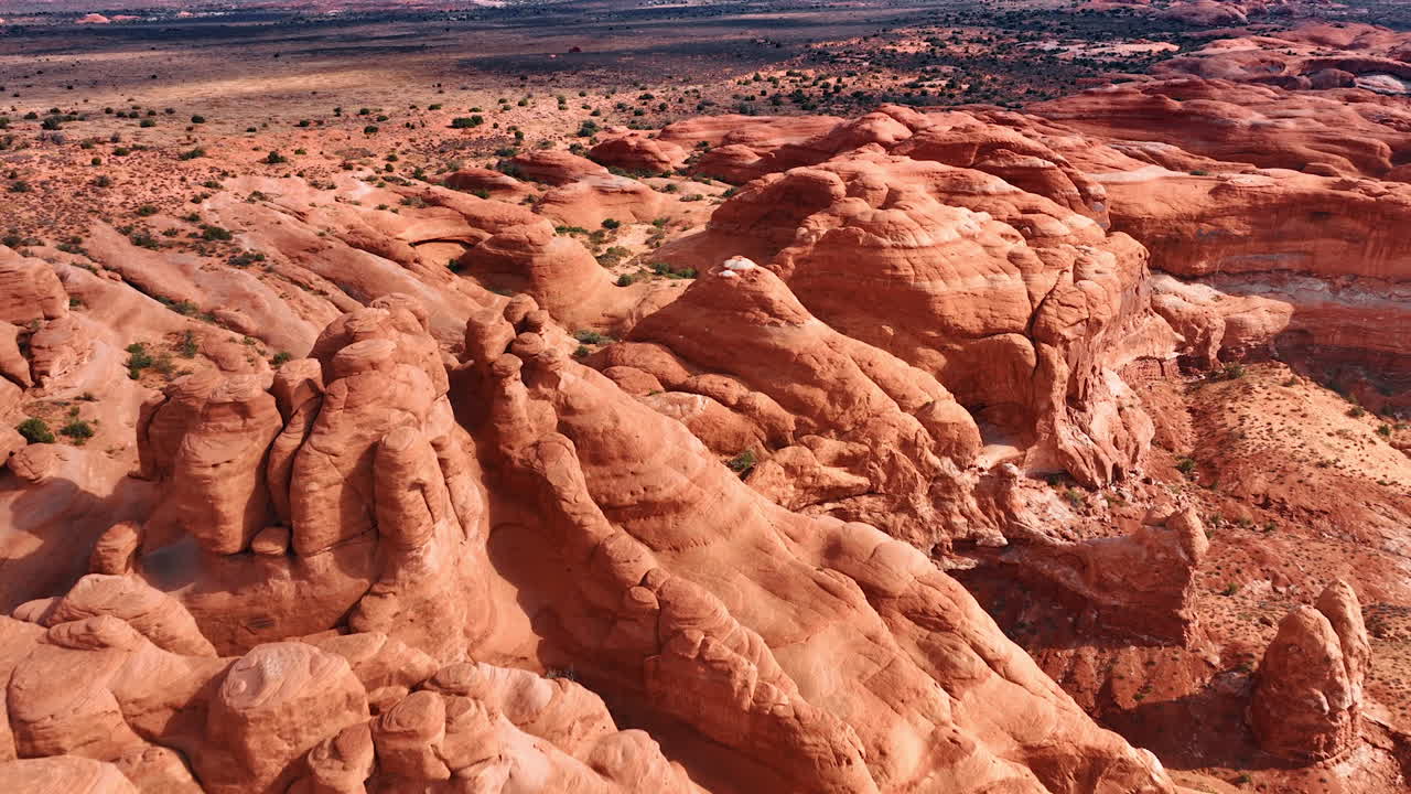 Filmato sopra le rocce rosse arrotondate e illuminate dal sole. Paesaggio desertico ricoperto di arbusti sullo sfondo. L'Arches National Park nello Utah, USA