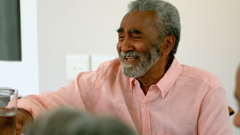 front view of senior black man toasting a glass of water at dining table in a comfortable home 4k