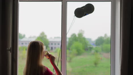 Housewife-drinks-tea-and-looks-at-robot-window-cleaner