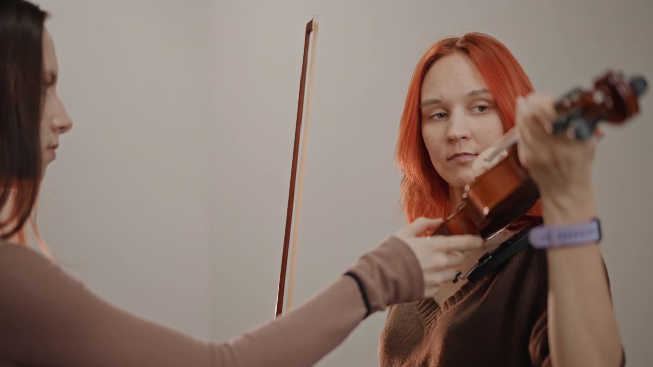 Lezione di violino femminile in un piccolo studio, l'insegnante regola lo strumento e l'archetto mentre la studentessa osserva, illuminazione calda, mani in primo piano, coaching di supporto, correzione della postura, tecnica passo-passo e calma.