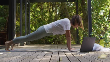 mujer asiática practicando yoga al aire libre en el jardín con computadora portátil