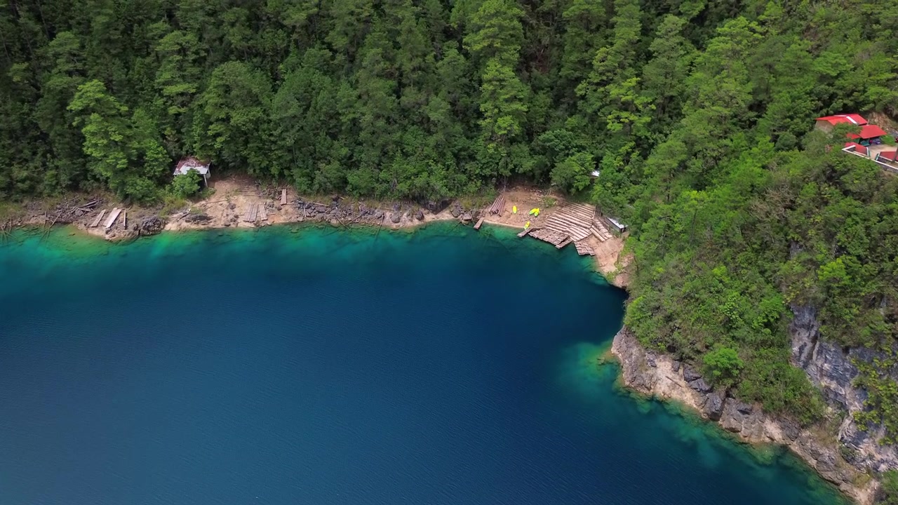 Ampia inquadratura aerea statica con drone della riva di un lago blu intenso e turchese con moli in legno e una baita dal tetto rosso nei Laghi di Montebello, Chiapas, Messico