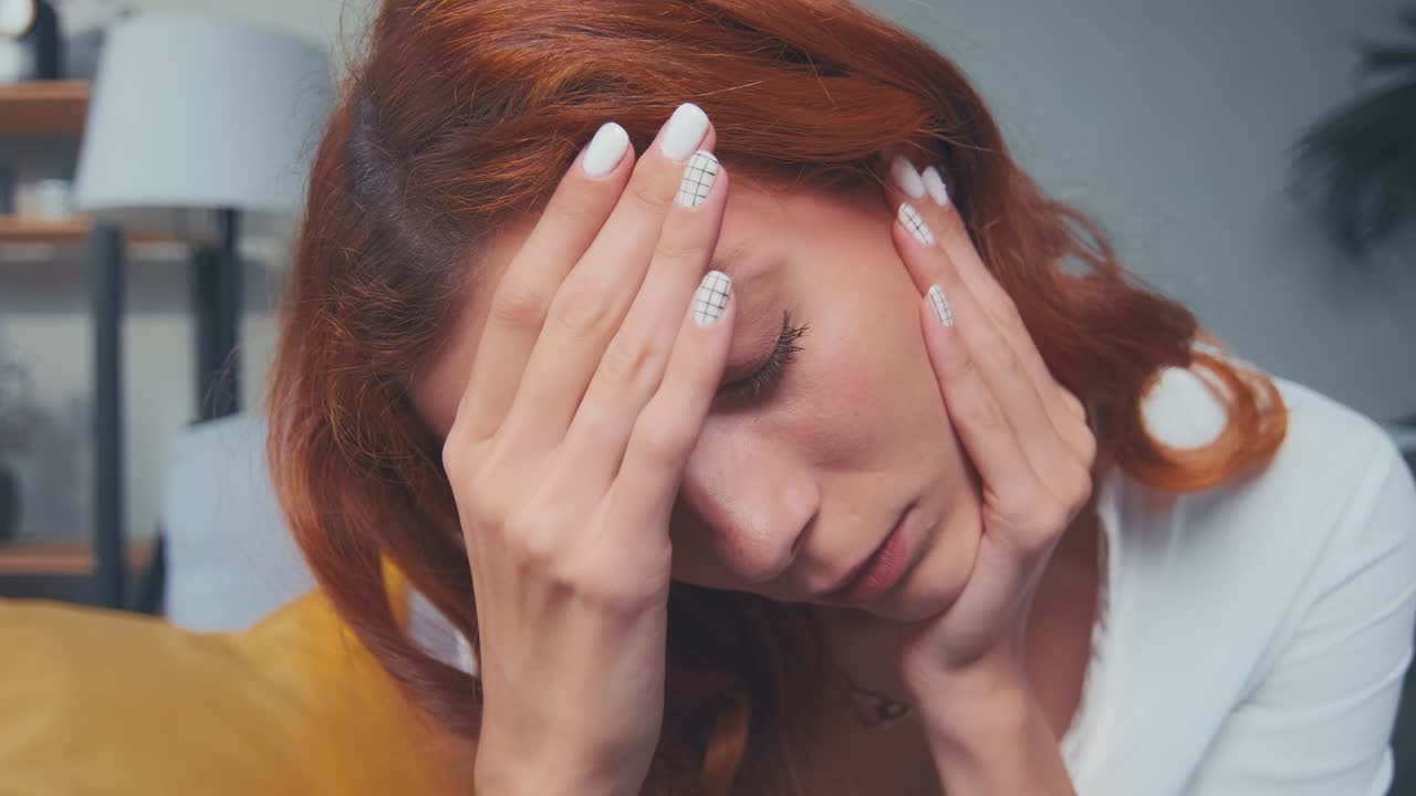 Sick tired exhausted redhead young woman coping with headache migraine at home