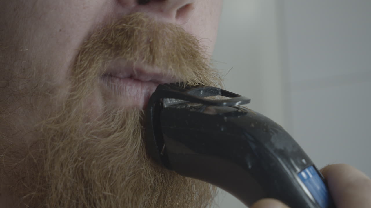 el hombre con una larga barba se afeita el bigote con una afeitadora eléctrica.