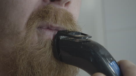 man with a long beard shaves his mustache with an electric razor