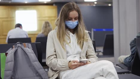 mujer turista con máscara de protección médica usando teléfono móvil en la terminal del aeropuerto