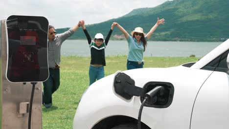 Concepto-De-Familia-Feliz-Progresiva-En-El-Parque-Eólico-Con-Vehículo-Eléctrico.