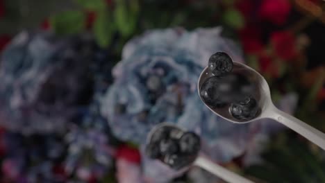 blueberries falling onto white spoon and bouncing off blue flower