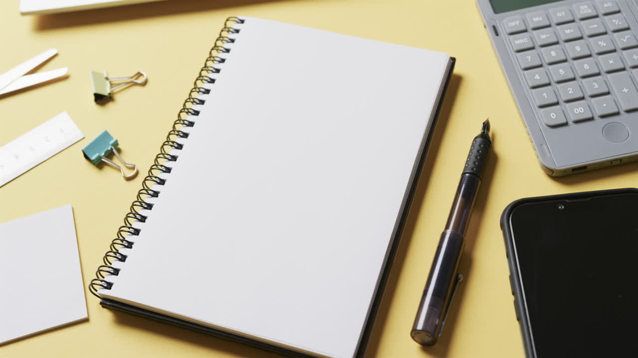Close up of notebook, smartphone and school stationery on yellow background, in slow motion
