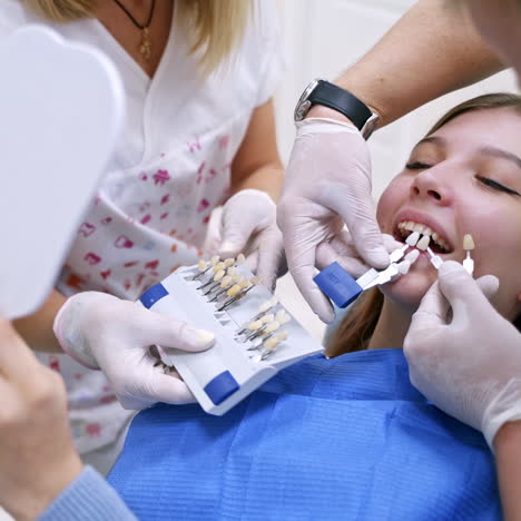 dentist holding artificial tooth close to patient's teeth. dentist with assistant select a color of tooth for the patient. progress of dental implantology.