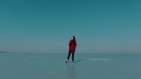 Tracking-front-shot-of-a-girl-ice-skating-on-a-frozen-lake-wearing-a-red-shawl,-on-a-clear-sunny-day,-serene-moments