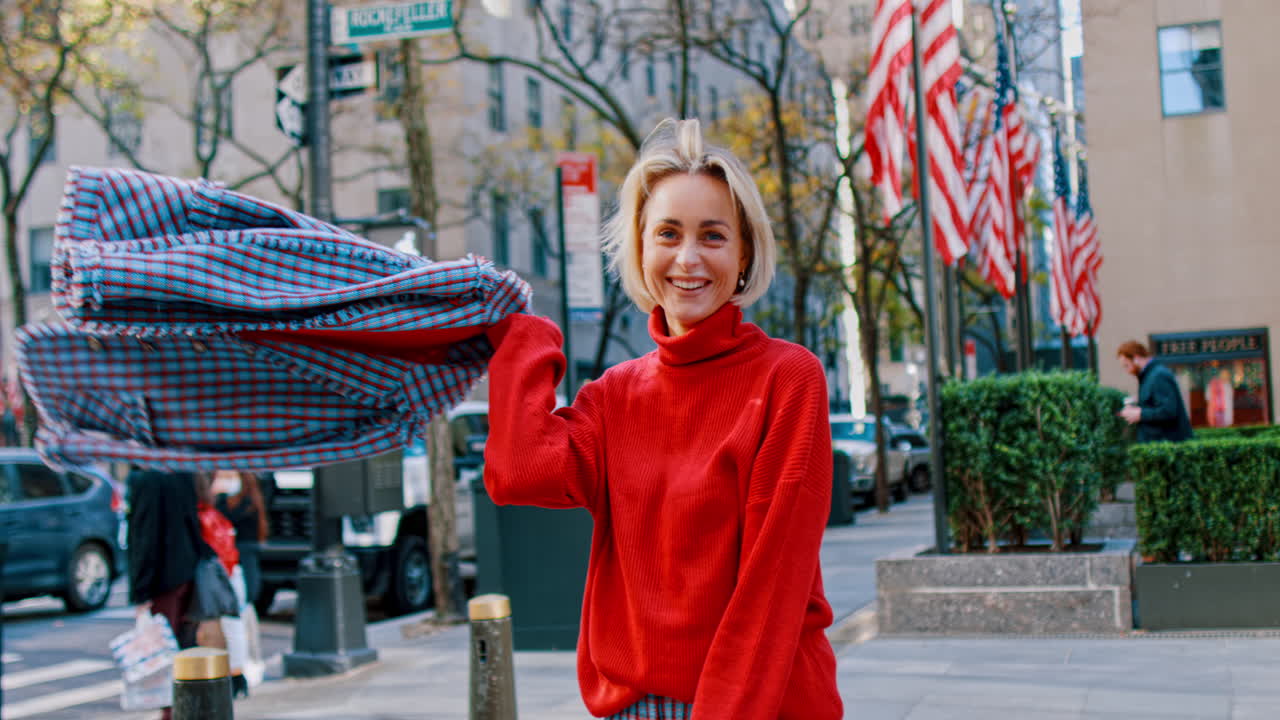 Nueva York, EE. UU., 5 de octubre de 2025: Mujer sonriente con suéter rojo en una calle de Nueva York. Una mujer feliz con un suéter de cuello alto rojo posa en una acera con banderas de fondo.