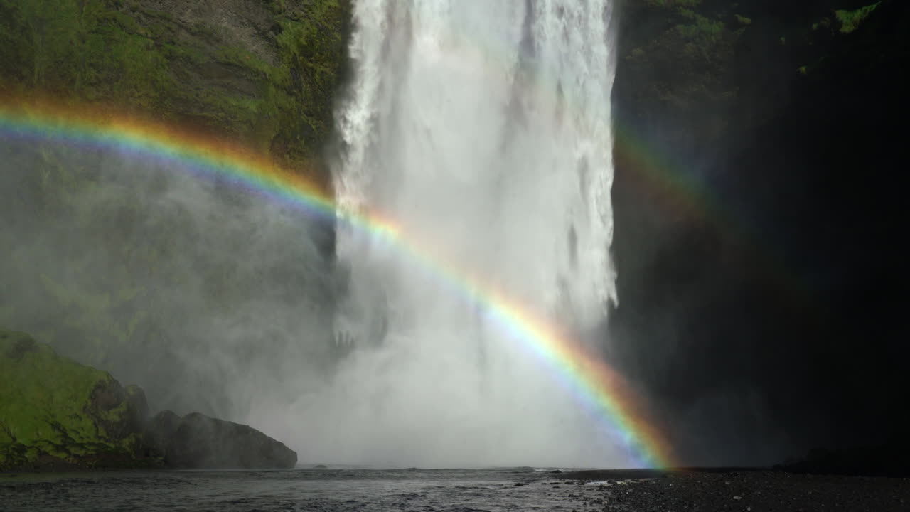 poderosa corriente que fluye desde escarpados acantilados rocosos con arco iris en skogafoss, skogar, islandia