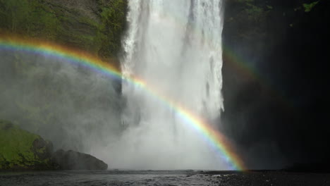 poderosa corriente que fluye desde escarpados acantilados rocosos con arco iris en skogafoss, skogar, islandia