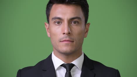 young handsome hispanic businessman against green background