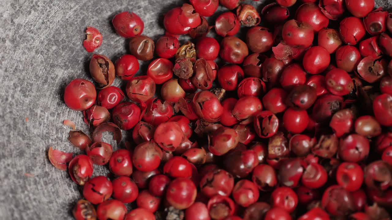 Dried pink pepper falling down in grey plate close-up. A bunch of natural pink pepper peas hot spice.Seasonings and condiments concept