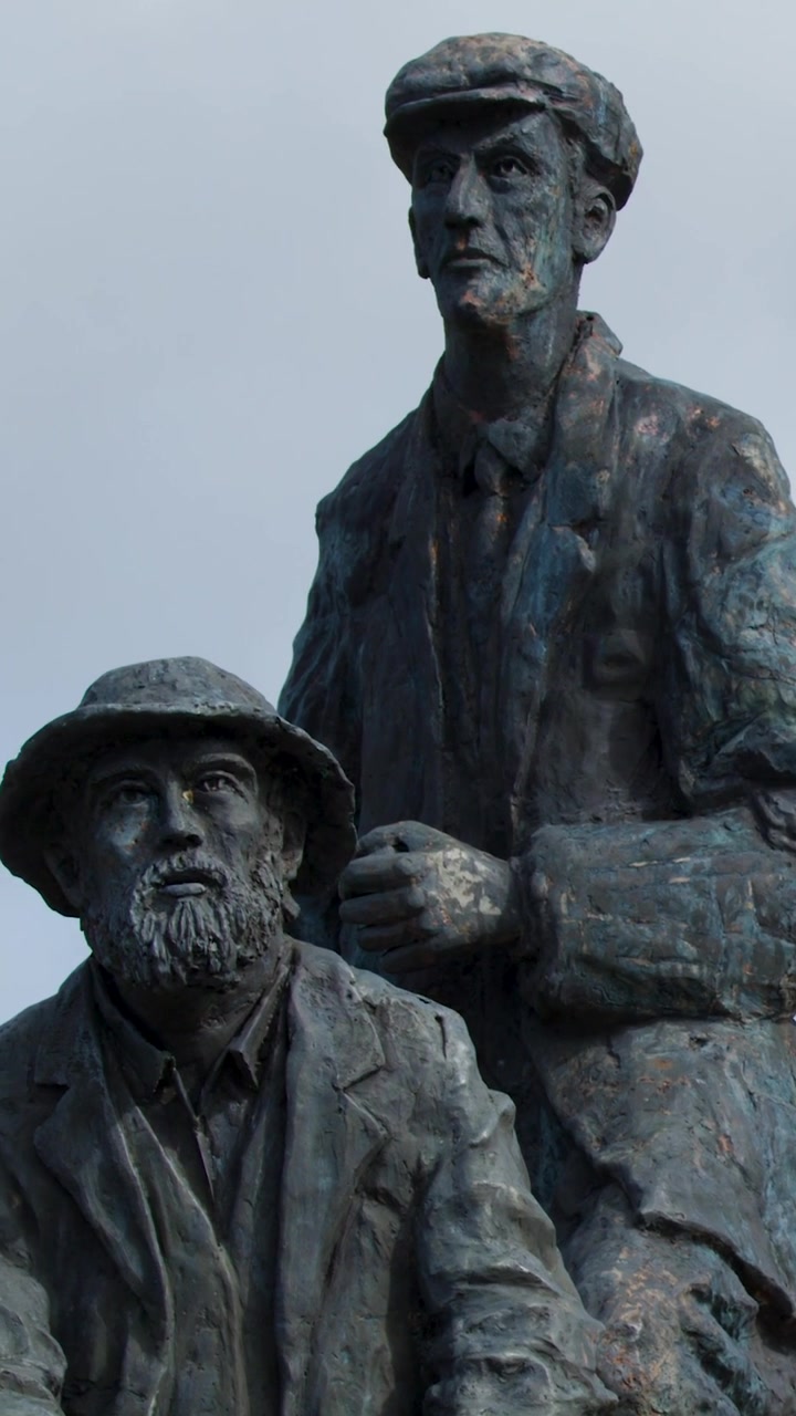 Un'inquadratura verticale dettagliata di una scultura commemorativa in bronzo che raffigura due uomini in abiti tradizionali.