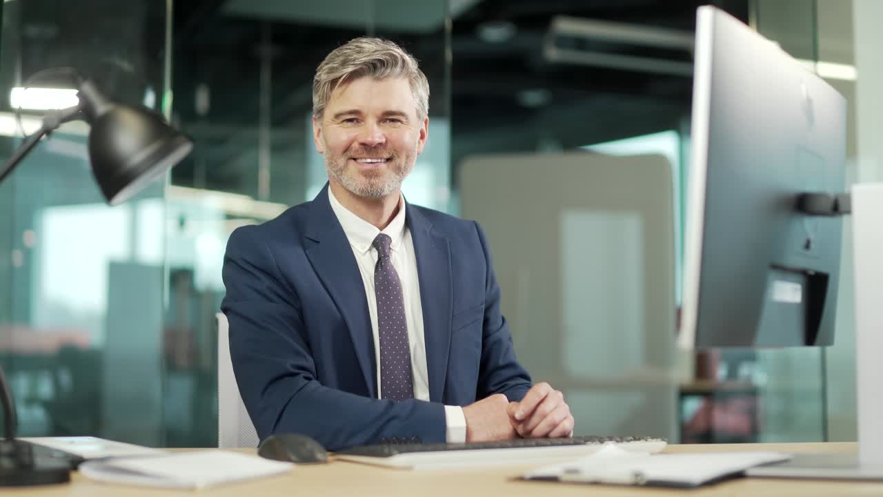 uomo d'affari maturo di successo che indossa un abito seduto a scrivania con un portatile in ufficio. ritratto di un uomo di capelli grigi di mezza età sicuro sul posto di lavoro che lavora al computer