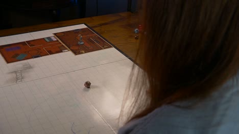 mujer rueda un troquel de metal de veinte caras en una alfombra de juego