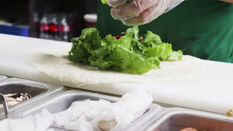 close up of a cook prepating a healthy green wrap with vegetables