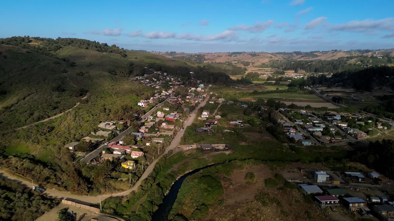 Zoom cinematico di un drone verso le case costiere e le verdi colline del villaggio di La Vega de Pupuya, vicino all'area umida in Cile