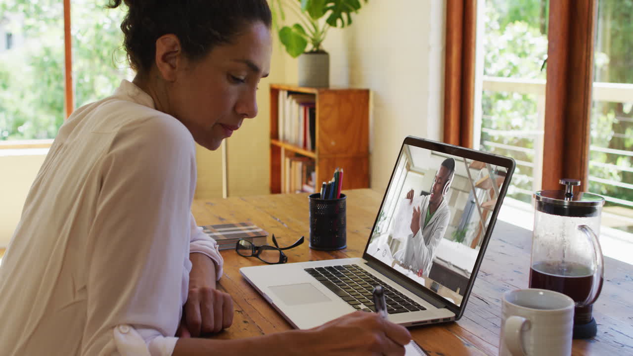 African american female teacher taking notes while having video call with college student on laptop