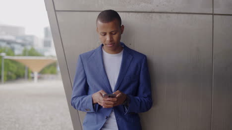 Joven-Sonriente-Apoyado-En-La-Pared-Y-Usando-Un-Teléfono-Inteligente.