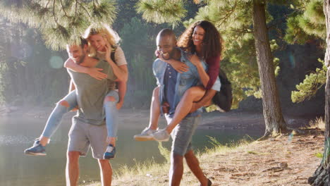 men giving women piggybacks as they walk beside lake together