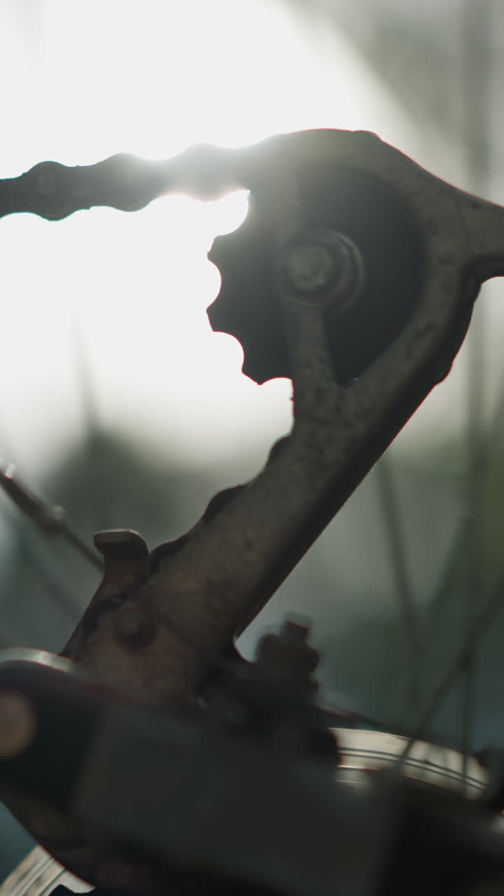 자전거의 뒷바와 기어 시스템의 클로즈업, 태양빛에서 천천히 회전하는 체인, 체인과 바가 날카로운 초점을 맞추고, 배경의 초록색이 부드럽게 흐릿합니다.