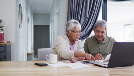 Happy-senior-biracial-couple-talking-and-using-laptop