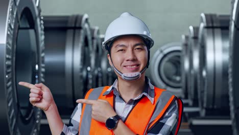 primer plano de un ingeniero masculino asiático con casco de seguridad sonriendo y señalando hacia un lado mientras estaba de pie en una fábrica de metal