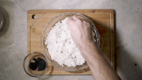 top down view on kitchen counter with a glass bowl of sushi rice and a hand dividing chai seeds on the dish as part of a recipe