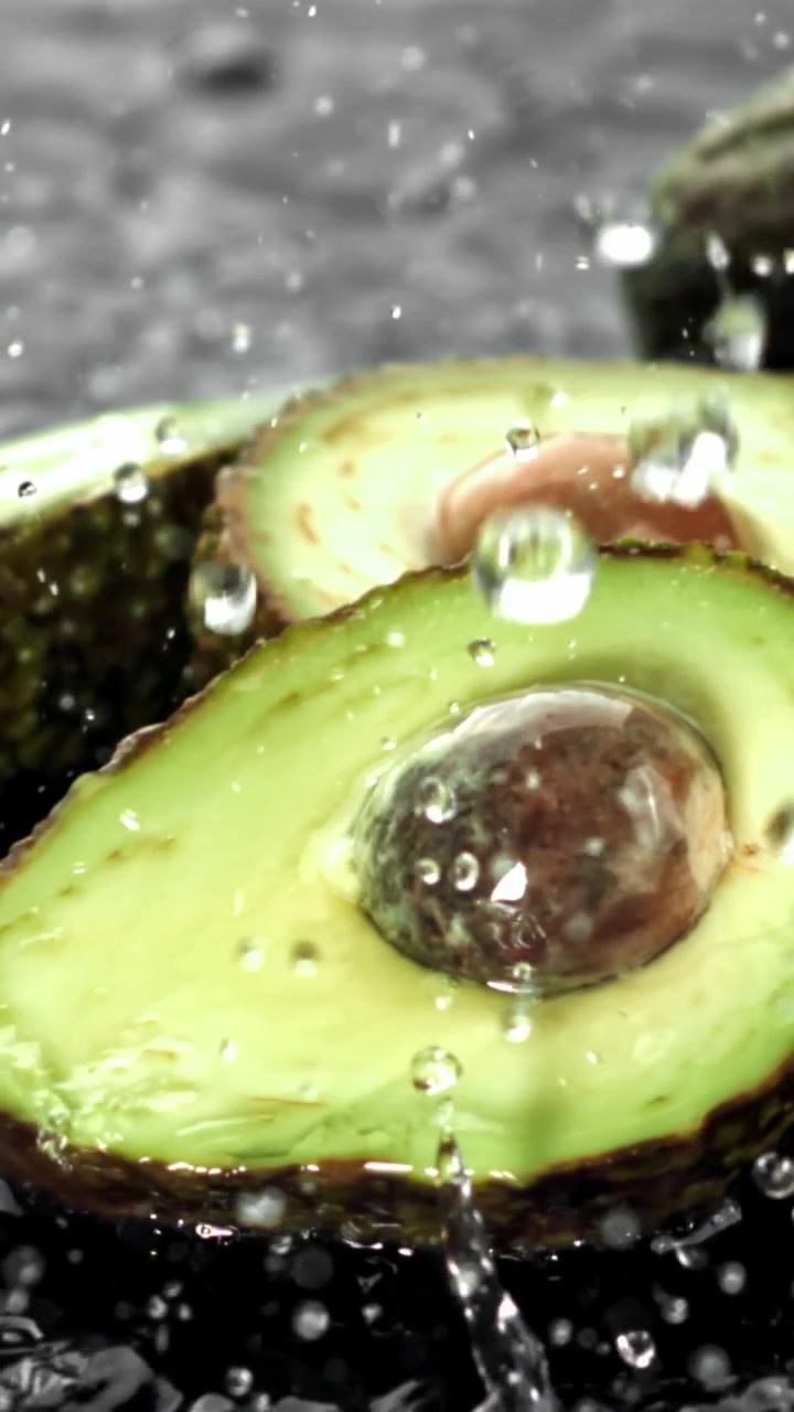 Schizzi d'acqua su metà di avocado freschi e verdi al rallentatore