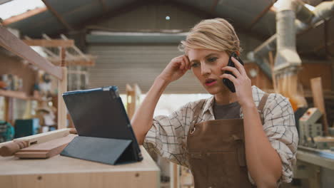 Frustrated-Female-Carpenter-With-Digital-Tablet-Working-In-Furniture-Workshop-Making-Phone-Call