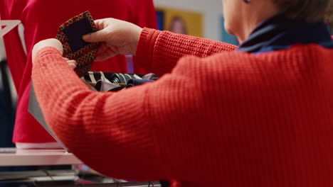 Elderly-woman-browsing-through-clothes-in-Christmas-decorated-shopping-store,-trying-to-pick-perfect-necktie-for-husband-as-xmas-present-during-winter-holiday-season,-close-up