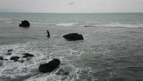 Pescador-Tratando-De-Pescar-En-La-Costa-Rocosa-De-Java-Occidental-Entre-Las-Olas-Del-Océano