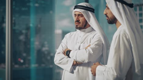 dos hombres de negocios musulmanes exitosos con trajes tradicionales blancos de pie en la oficina reuniéndose, negociando y hablando sobre oportunidades financieras. saudi, emirati, concepto de hombre de negocios árabe.