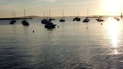 boats silhouetted on golden shimmering harbour ocean surface aerial view dolly right