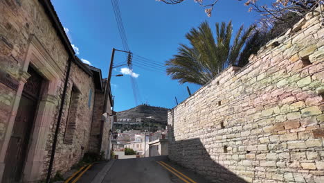 vista hacia arriba de una calle estrecha en lefkara con paredes de piedra y palmera